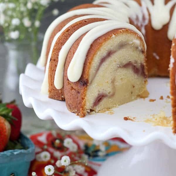 A Strawberry Swirl Bundt Cake with a slice taken out of it on a white cake plate with scallop edges