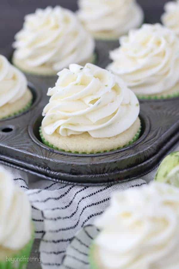 A cupcake sitting in a vintage cupcake pan with a white frosting and lime zest