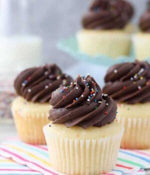 Three yellow cupcakes stacked together. These cupcakes are topped with chocolate frosting and sprinkles.