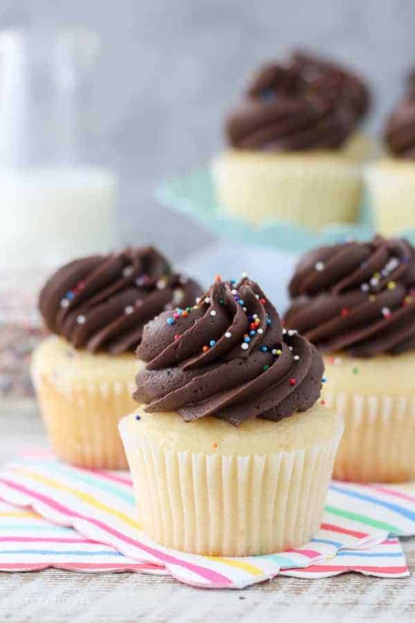 Three yellow cupcakes stacked together. These cupcakes are topped with chocolate frosting and sprinkles.