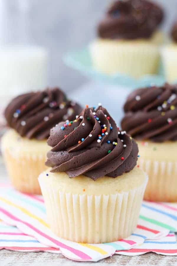 A close up shot of a perfect yellow cupcake with a big swirl of chocolate frosting and sprinkles