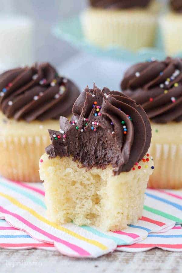 A giant bite taken out of this yellow cupcake covered with chocolate frosting and sprinkles