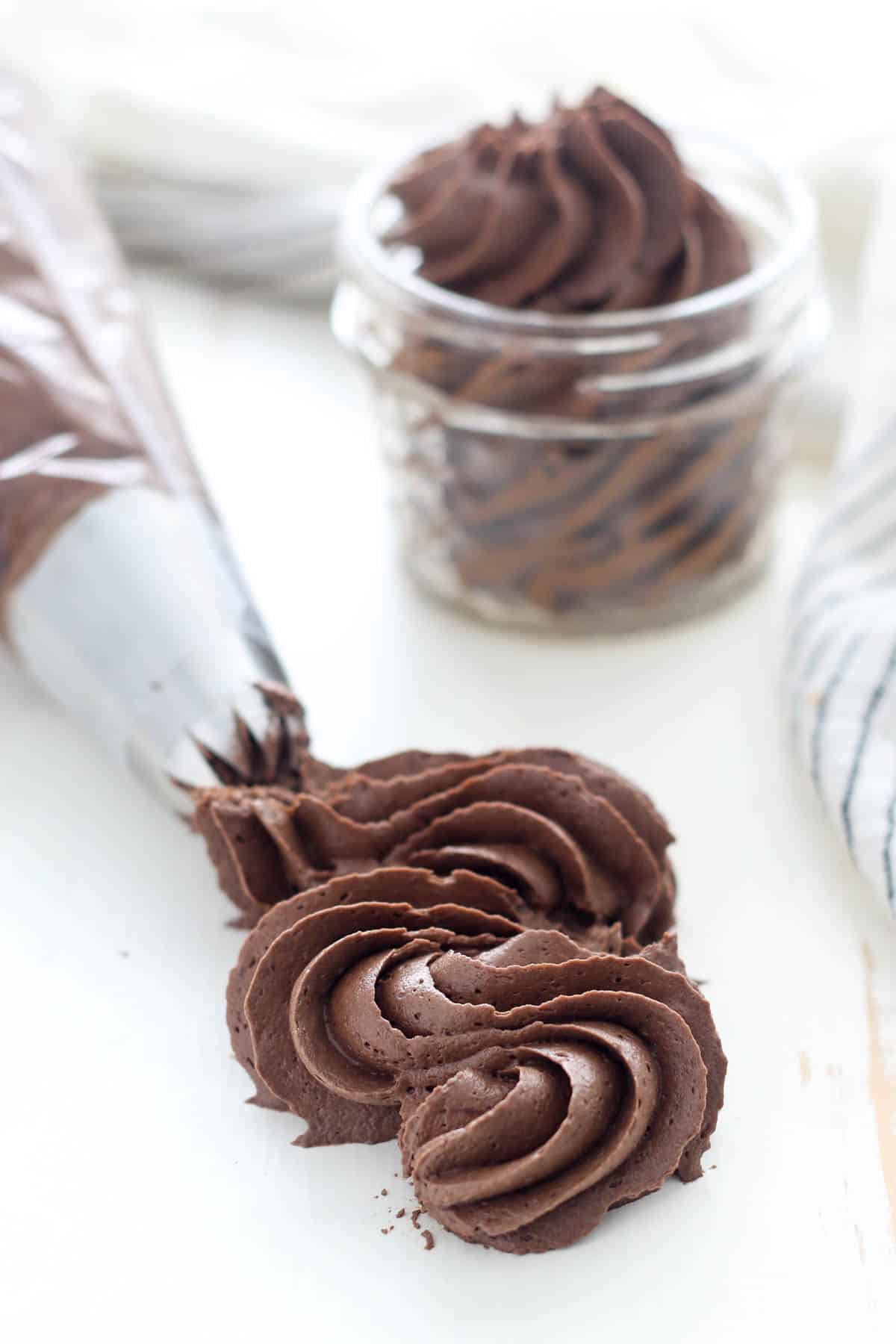 Piping tip with a swirl of chocolate frosting, and chocolate frosting in a jar.