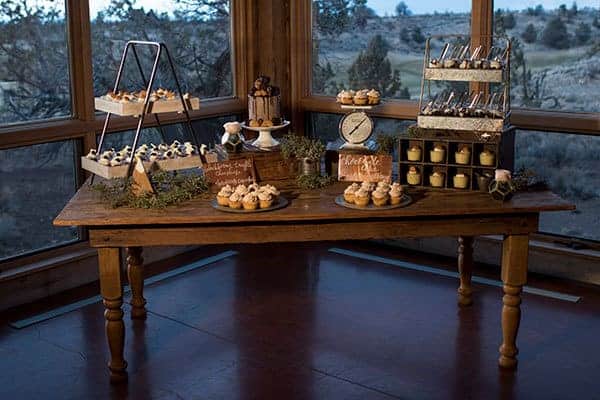 A rustic dessert table for a barn-themed wedding features pieces using varying heights, wooden boxes and cake stands at Brasada Ranch in Powell Butte Oregon