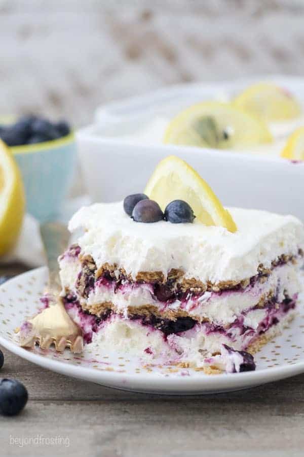 A layered icebox cake with blueberries and graham crackers on a gold polka dot plate. There's a few bites missing.