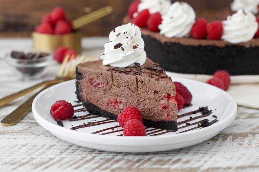 A large chocolate cheesecake garnished with whipped cream chopped chocolate and raspberries.