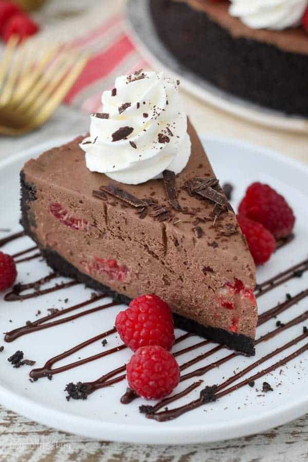 A big slice of chocolate cheesecake on a white plate drizzled with chocolate and garnished with raspberries