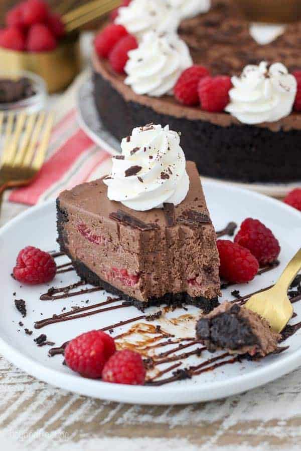 A white plate with a message chocoalte drizzle, raspberries and a slice of cheesecake with a couple large bites taken out of it