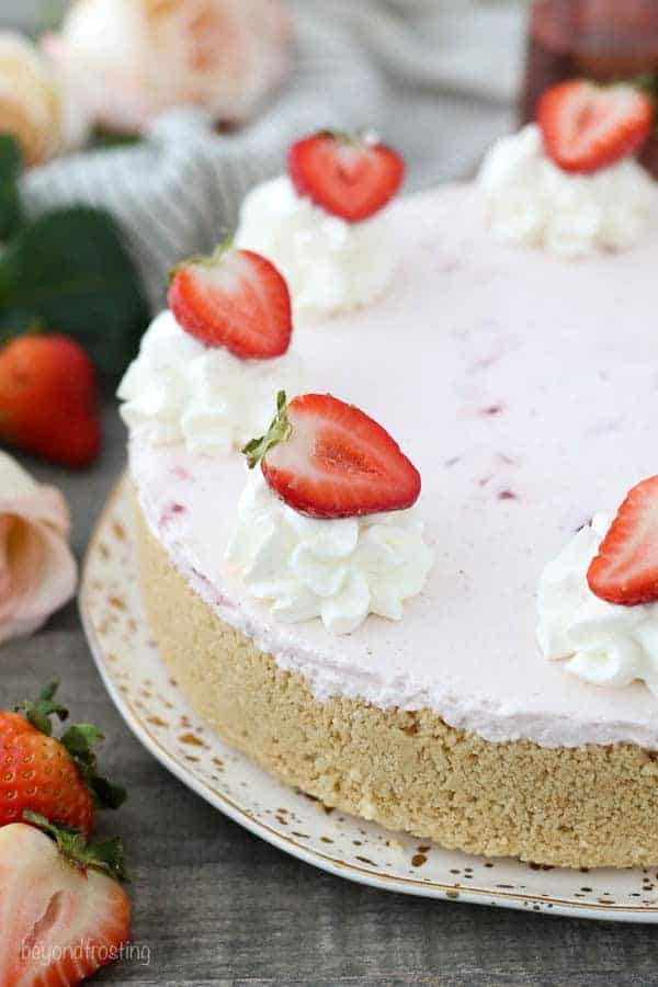 A whole mousse cake cake on a gold polka dot plate garnished with strawberries and whipped cream