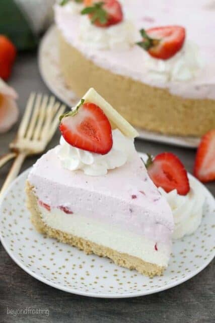 A slice of mousse cake with two layers, the bottom layers is white chocolate and the top layer is strawberry. It's decorated with whipped cream, strawberries and white chocolate.