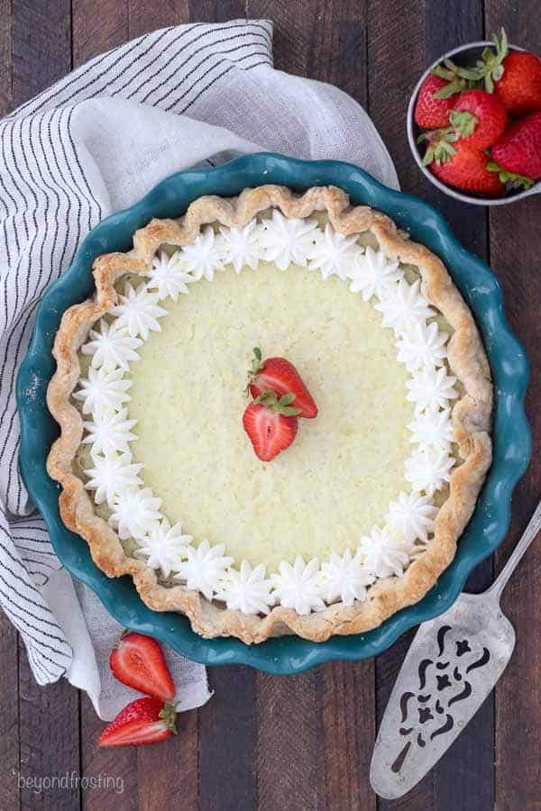 An overhead view of a whole coconut pie with dollops of whipped cream and two strawberries in the middle