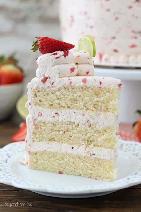 A tall slice of layer cake with a fresh strawberry frosting. Garnished with strawberries and limes