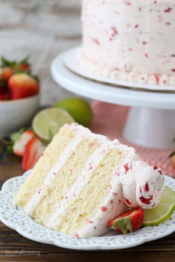 A slide of margarita cake with strawberry frosting on a white plate with a slice of strawberry and a slice of lime