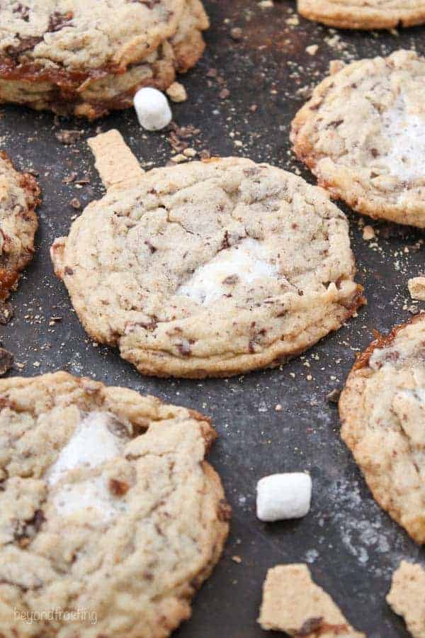 A bunch of cookies laid out on a cookie sheet with a lot of crumbs and mini marshmallows
