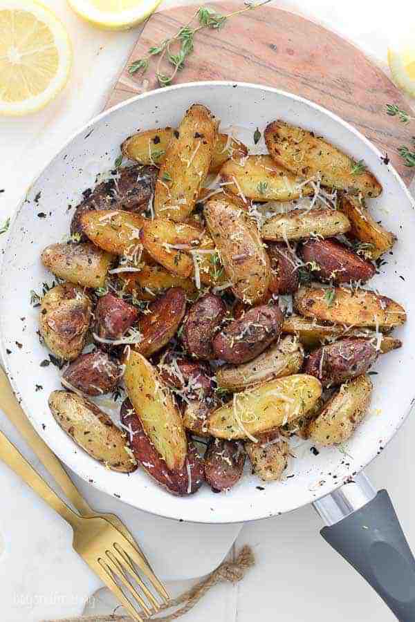 An overhead shot of a skillet with roasted lady fingerling potatoes garnished with parmesan and fresh thyme