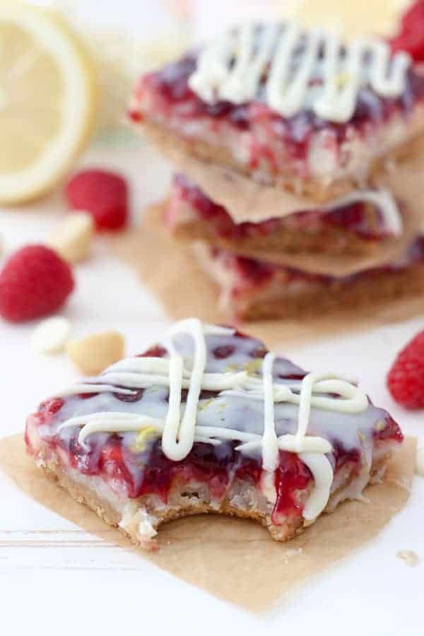 A raspberry bar sitting on a brown piece of parchment paper with a bite taken out of it.