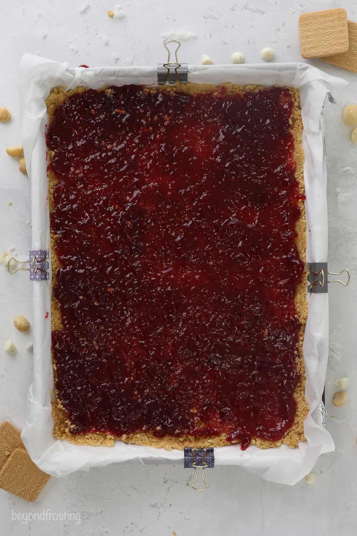 Raspberry jam spread over a shortbread crust in a large baking pan.