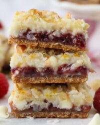 A stack of three raspberry lemon magic bars on a countertop next to raspberries and white chocolate chips.
