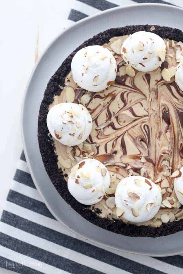 An overhead shot of a mocha fudge pie on a white cake plate with ribbons of fudge swirl, whipped cream and garnished with sliced almonds