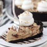 A fork sinking into a slice of mocha pie with large layers of fudge sauce. The pie is garnished with whipped cream and sliced almonds.