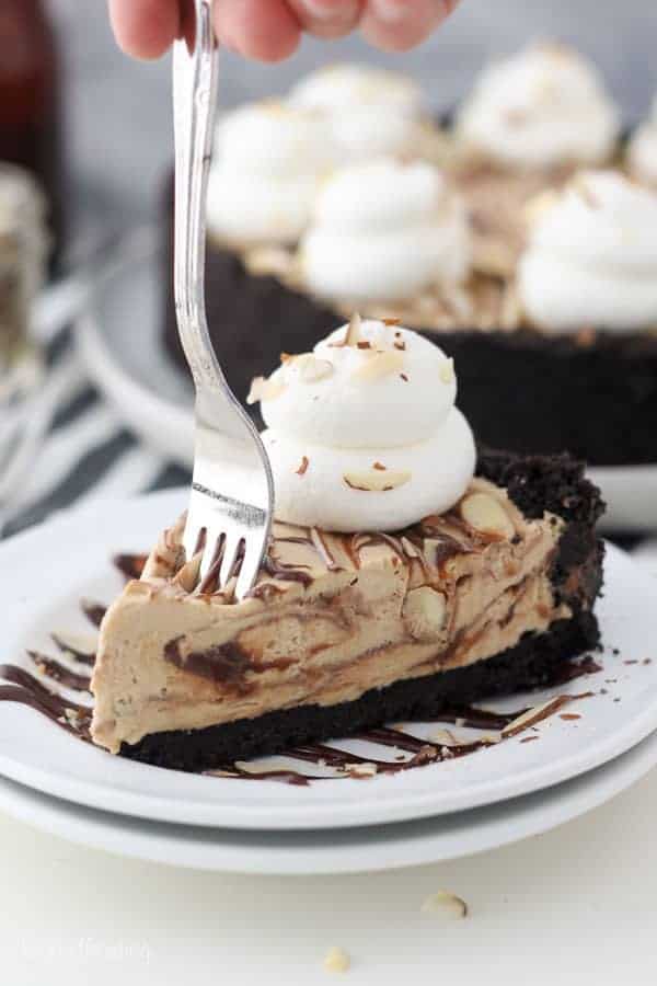 A fork sinking into a slice of mocha pie with large layers of fudge sauce. The pie is garnished with whipped cream and sliced almonds.