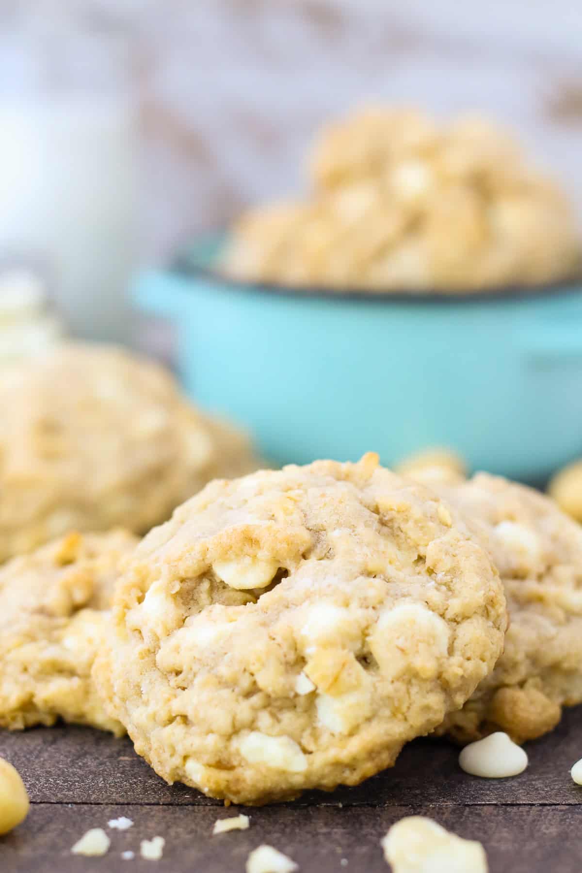 These chunky, no-chill oatmeal macadamia nut cookies are soft, chewy, and loaded with salty macadamia nuts and creamy white chocolate chips. Oatmeal white chocolate macadamia nut cookies on a countertop with a bowl of cookies in the background.