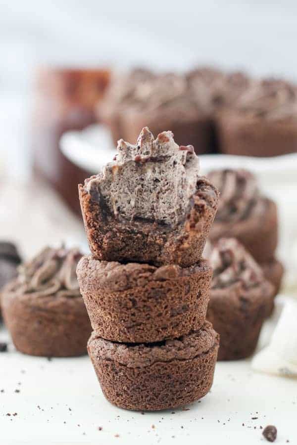 A tall stack of 3 cookie cups, the cookie cup on top is filled with an cheesecake filling and there's a big bite taken out of it