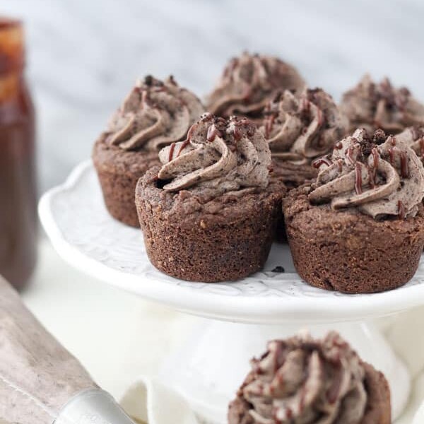 A group of chocolate cookie cups on a white cake plate with an Oreo filling and chocolate drizzle