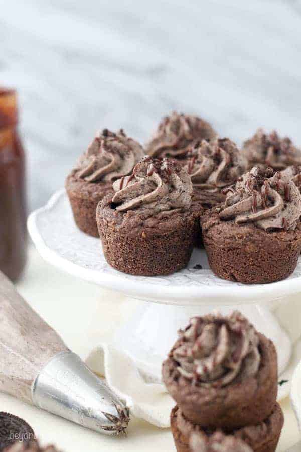 A group of chocolate cookie cups on a white cake plate with an Oreo filling and chocolate drizzle