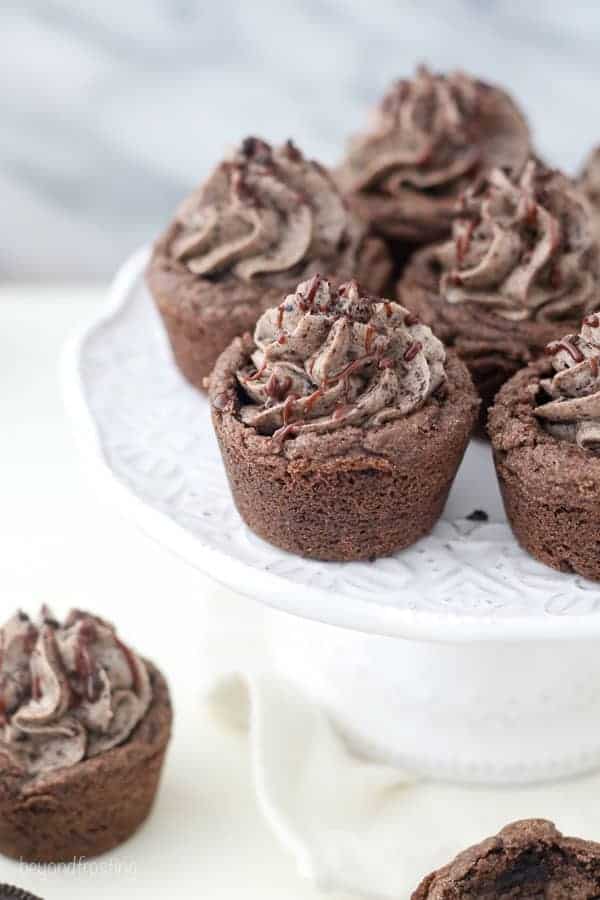 Mini Oreo cookie cups on a white cake stand drizzled with chocolate and crushed Oreos