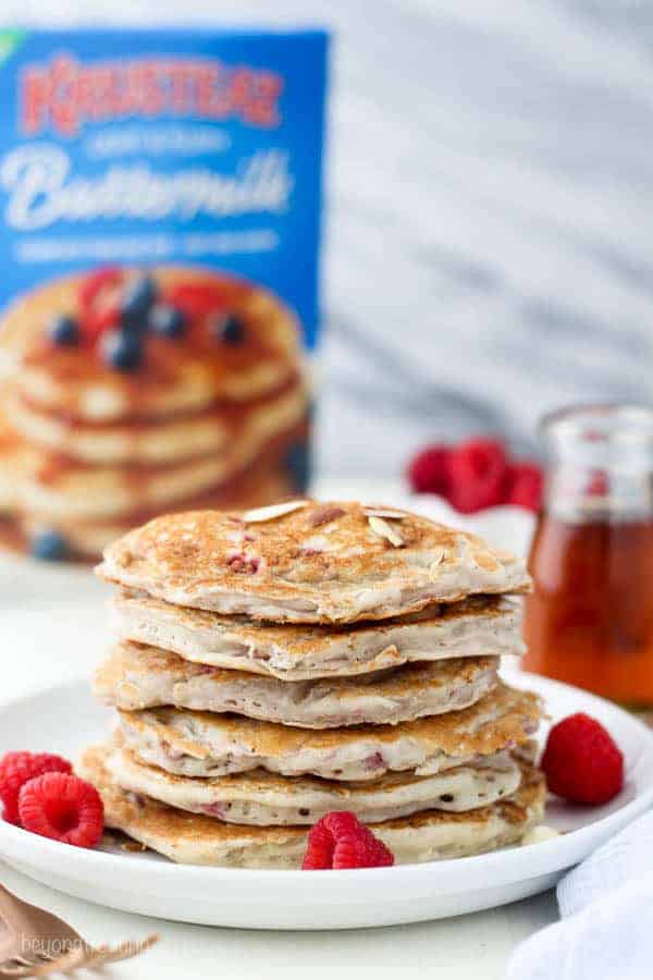 A big stack of raspberry pancakes with a box of Kusteaz Buttermilk Pancakes mix in the background