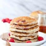 A big stack of buttermilk raspberry pancakes on a white rimmed plate