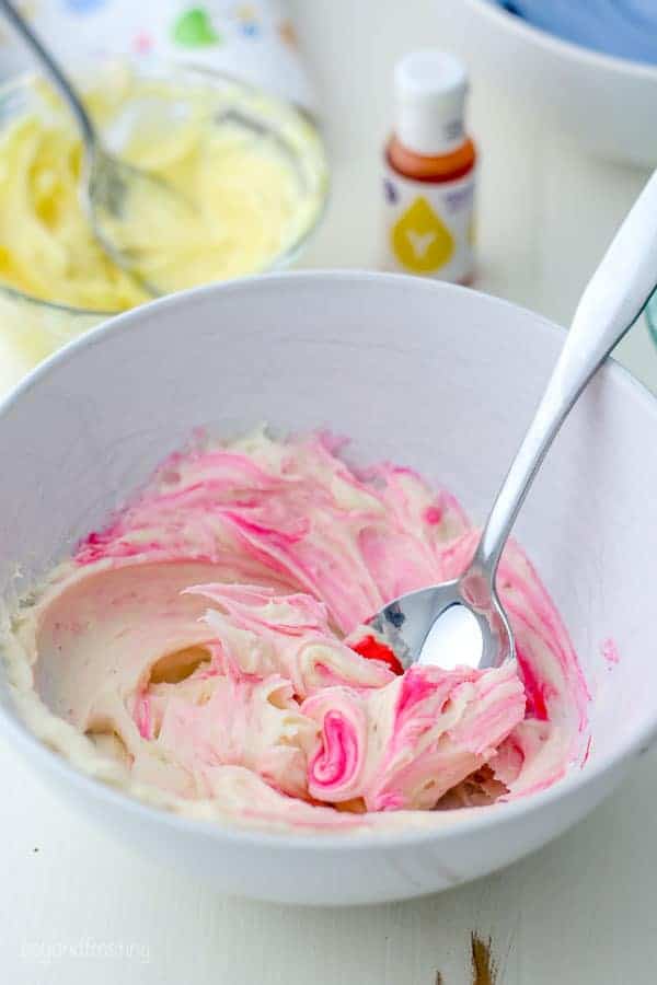 Un bol blanco lleno de glaseado de vainilla que se tiñe de rosa. El color rosa se arremolina en el glaseado