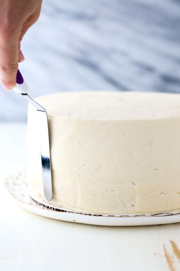 An angled spatula is pressed up again the edges of the cake to get nice and smooth edges