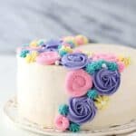 A side view of a layer cake with white frosting and colorful buttercream flowers