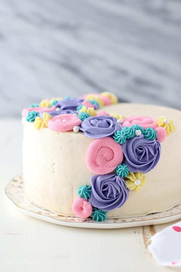 A side view of a layer cake with white frosting and colorful buttercream flowers