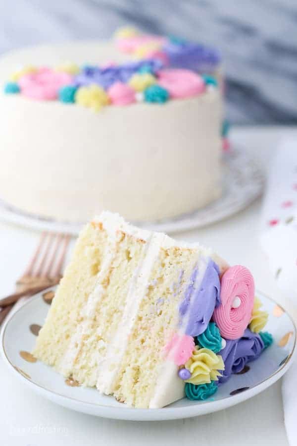 A large slice of a vanilla layer cake on a white plate with gold polka dots