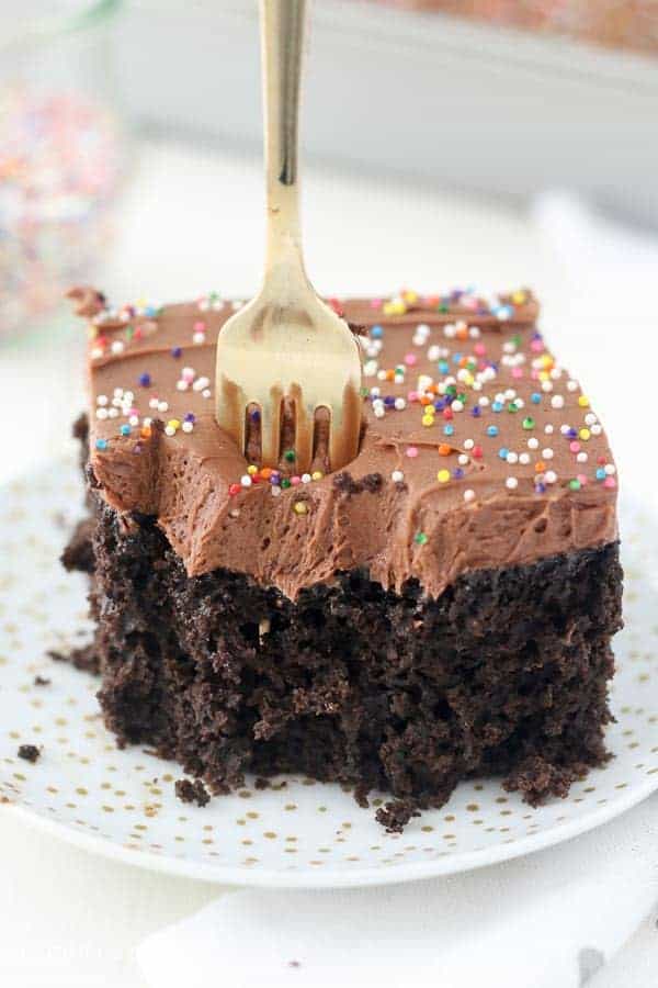 Un tenedor dorado que se hunde en una rebanada de pastel de chocolate con chispas de colores.