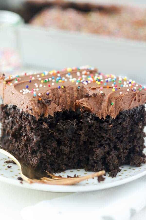 A close up shot of a half-eaten slice of dark chocolate cake with a chocolate frosting and sprinkles.