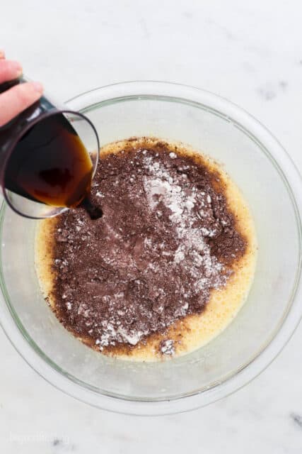 Coffee is poured into a glass bowl with cocoa powder and flour added to wet batter ingredients.