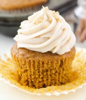 A pumpkin cupcake with cream cheese frosting with the wrapper pulled off