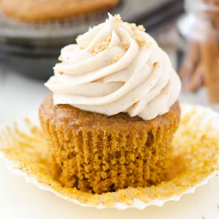A pumpkin cupcake with cream cheese frosting with the wrapper pulled off