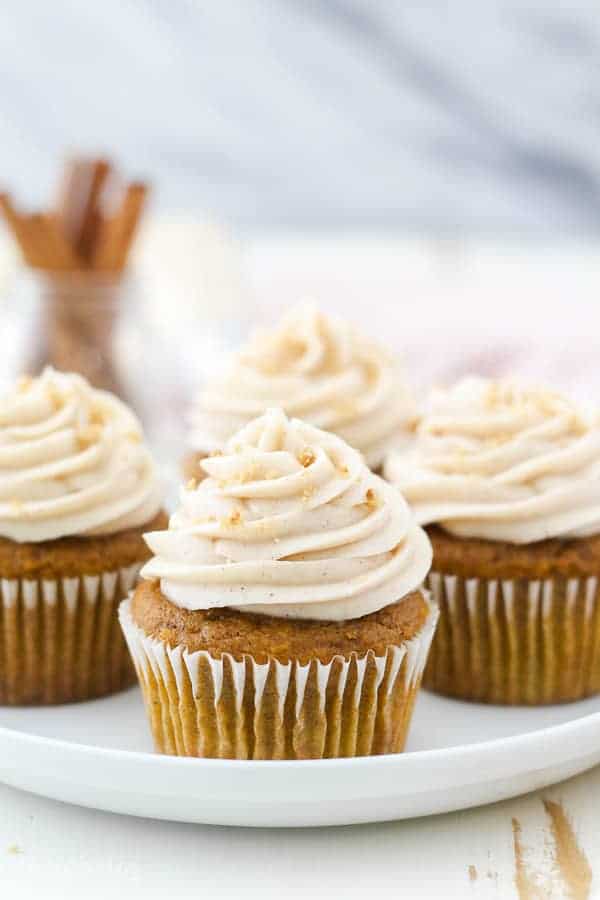 A head on view of 4 pumpkin cupcakes on a white rimmed plate with a beautiful frosting