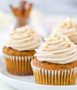 A close up shot of a pumpkin cupcake topped with a swirl of cream cheese frosting