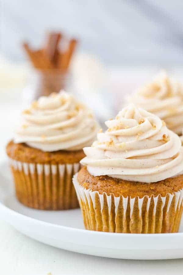 A close up shot of a pumpkin cupcake topped with a swirl of cream cheese frosting