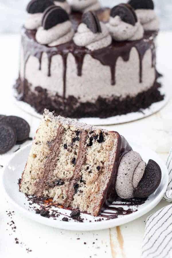A big slice of Oreo cake on white rimmed plate with chocolate frosting and Oreo buttercream