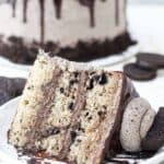 A giant slice of cake on a white rimmed plate. The cake is loaded with crushed Oreos and there's a big dollop of Oreo frosting on top