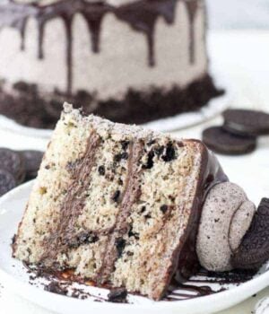 A giant slice of cake on a white rimmed plate. The cake is loaded with crushed Oreos and there's a big dollop of Oreo frosting on top