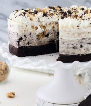 An Oreo brookie mousse cake with a large slice missing on a white cake stand.