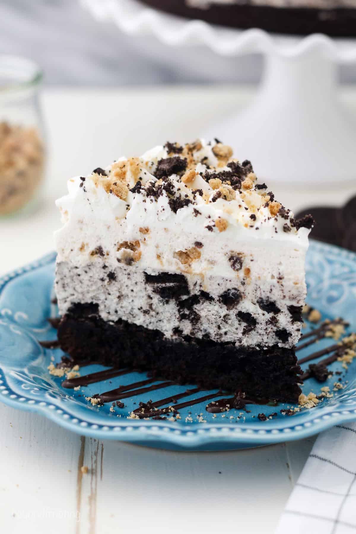 This easy brookie mousse cake recipe has a fudgy brownie bottom layered with creamy Oreo cheesecake and fluffy chocolate chip cookie mousse! A slice of Oreo brookie mousse cake on a blue plate.